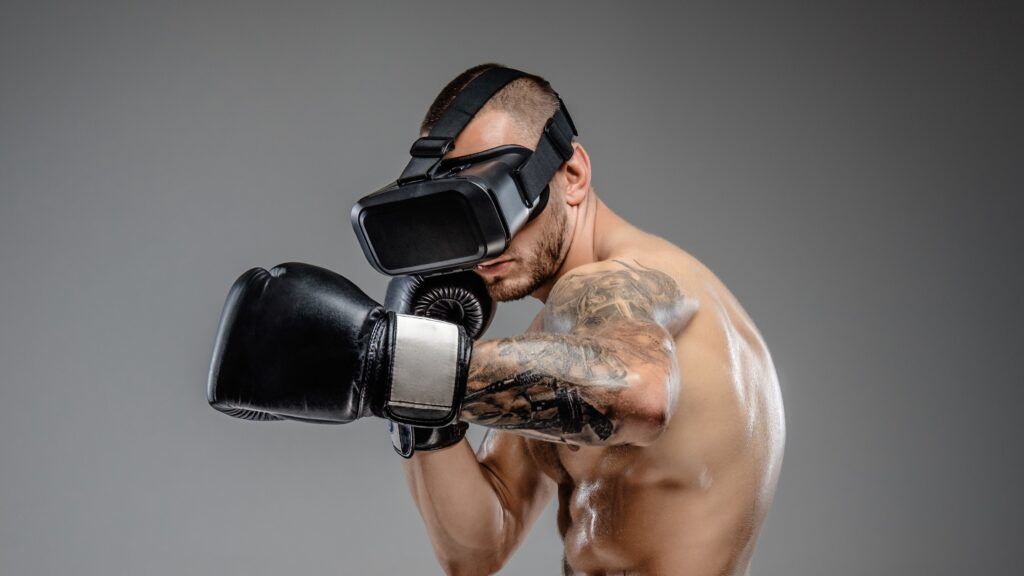 Shirtless brutal boxing fighter in virtual reality glasses on his head. Isolated on a grey background.