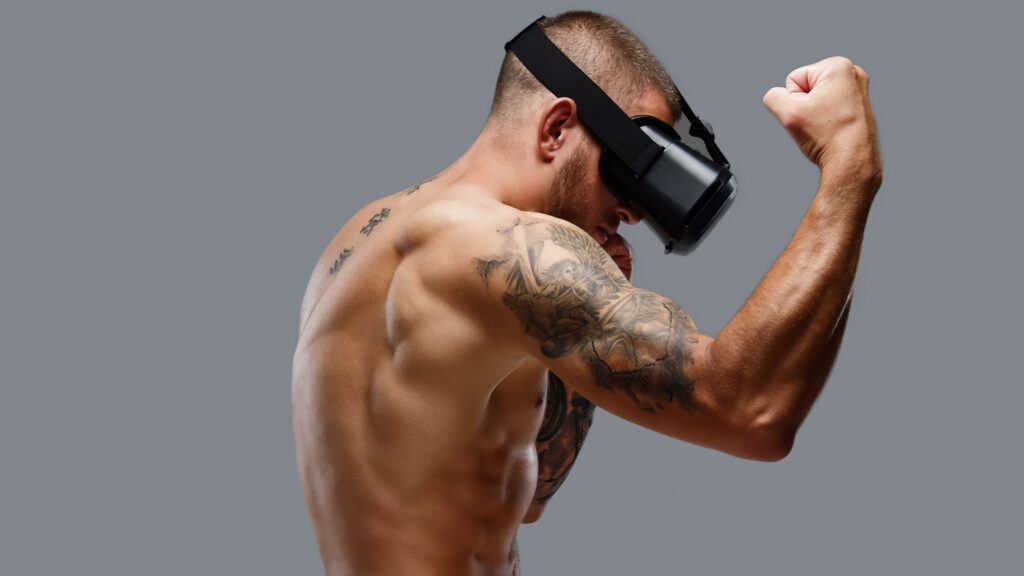 Shirtless brutal boxing fighter in virtual reality glasses. Shirtless brutal boxing fighter in virtual reality glasses on his head. Isolated on a grey background.