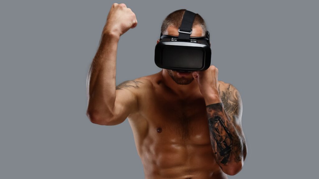 Shirtless brutal boxing fighter in virtual reality glasses. Shirtless brutal boxing fighter in virtual reality glasses on his head. Isolated on a grey background.